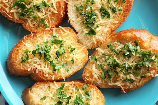 Вкусные ломтики хлеба с тертым сыром, чесноком и зеленью на тарелке
