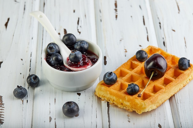 Tasty breakfast. Belgian waffles with whipped cream blueberries and jam on a wooden white