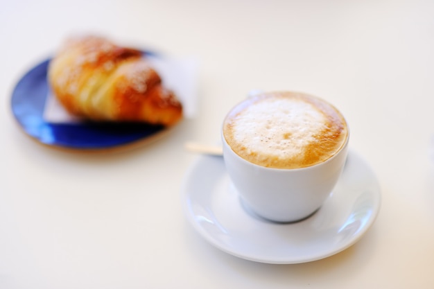 Tasty breakfast in a italian street cafe - cup of coffee and croissant on white table