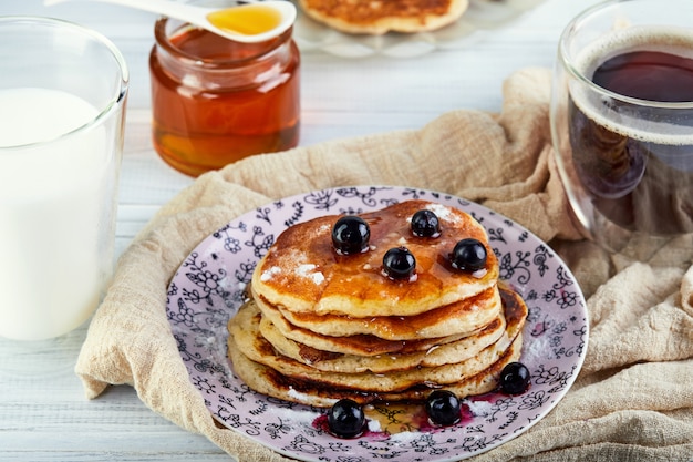 Tasty breakfast. A stack of pancakes with honey syrup a glass of milk, espresso coffee and honey on a wooden white