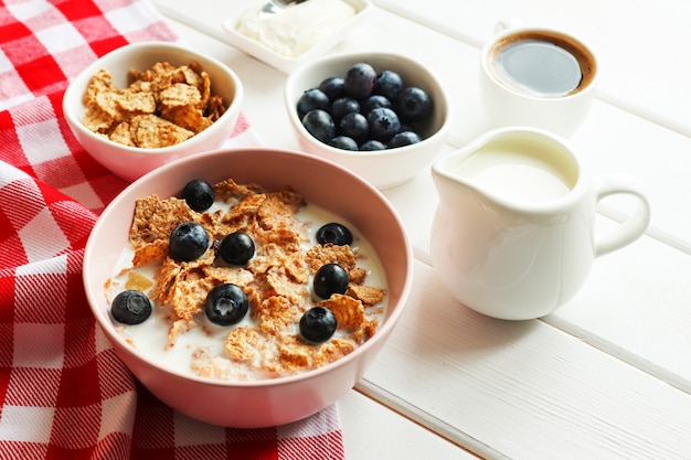 Tasty breakfast of whole wheat flakes with milk blueberries and cup of coffee closeup on wooden table