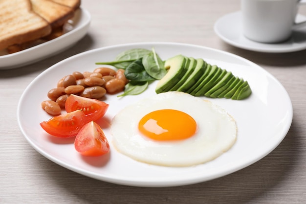 Tasty breakfast with fried egg beans and avocado served on white wooden table closeup