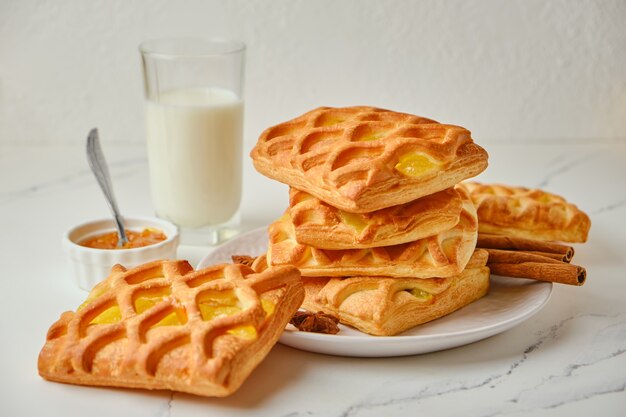 Tasty breakfast with puff pastry mini pies with pear and lime jam filling and a glass of milk on white table