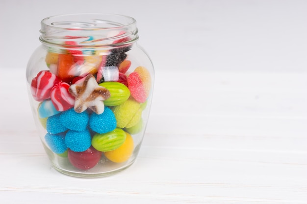 Photo tasty bright chewing sweets and jelly candies in the glass can on wooden white board