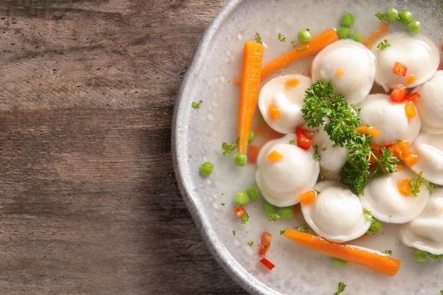 Tasty broth with dumplings on wooden table