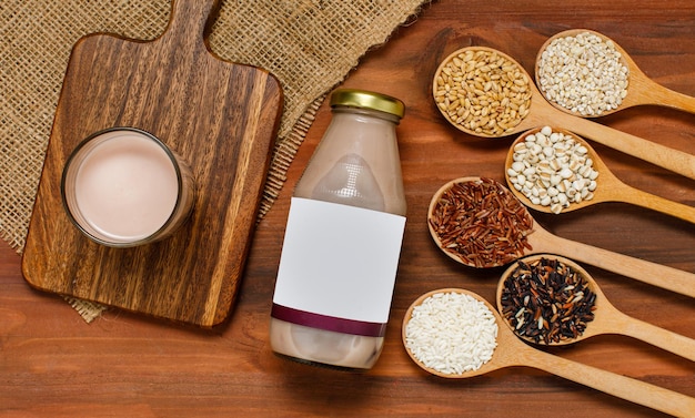 Tasty brown rice milk in drink glass and bottle on kitchen table with spoon of organic ingredient grain. Natural nourishment cereal for health care and vitamin supplement served as traditional dessert