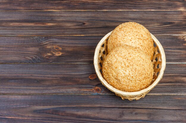 Tasty bun with basket bread on wooden background