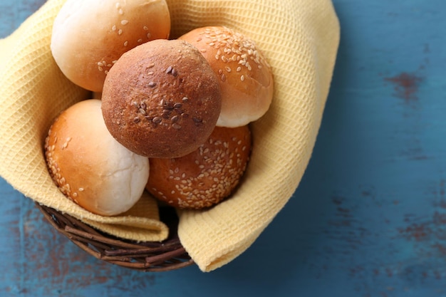 Tasty buns with sesame in wicker basket on color wooden background