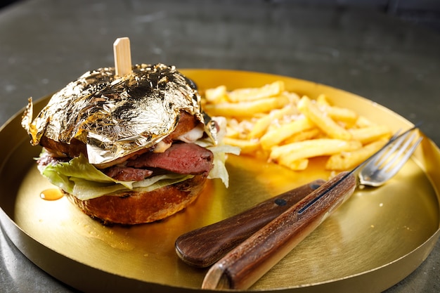 Tasty burger cheeseburger with tomato, lettuce and veal cutlets on white rustic wooden table, close-up, selective focus