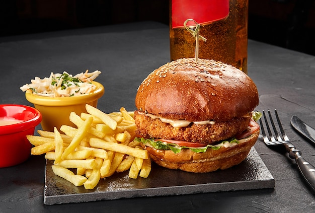 Tasty burger french fries with sauce and glass of beer on black board