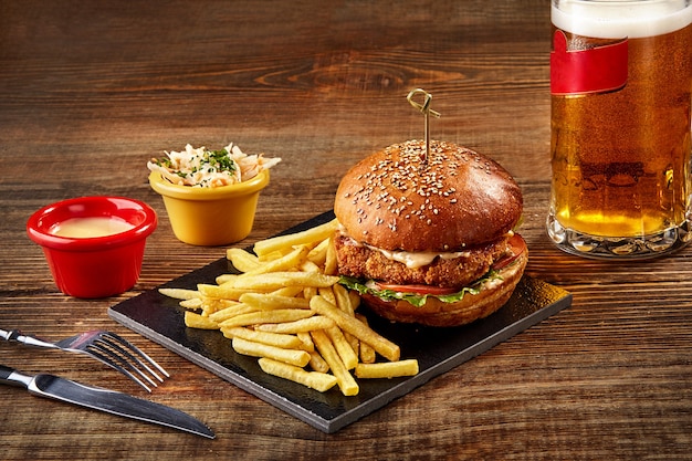 Tasty burger french fries with sauce and glass of beer on black board