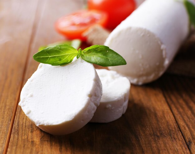 Photo tasty bushe cheese with basil and tomato on wooden table