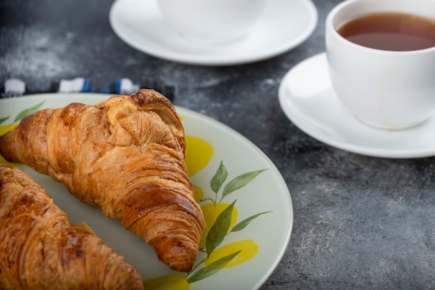 Tasty buttery croissants with cups of tea on stone table .