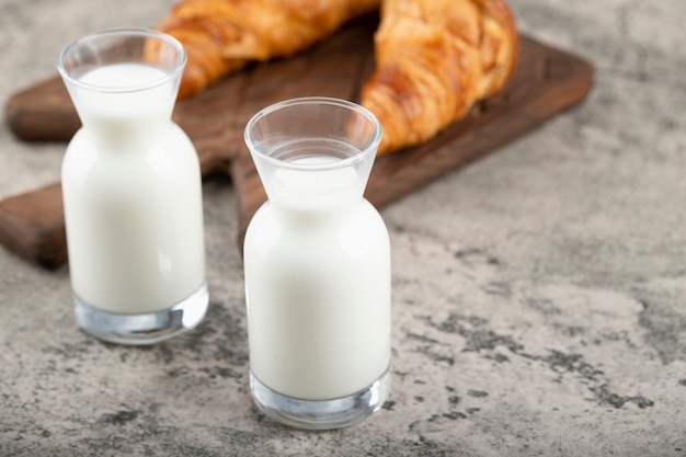 Tasty buttery croissants with glass pitchers of fresh milk placed on stone table .