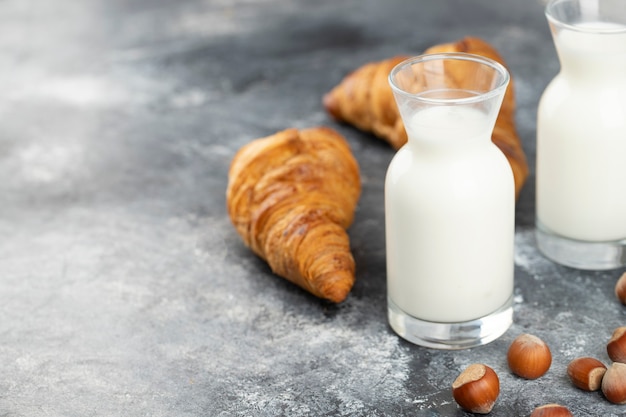 Tasty buttery croissants with glass pitchers of milk and hazelnuts on stone table .