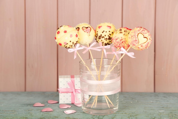 Tasty cake pops and gift on wooden background