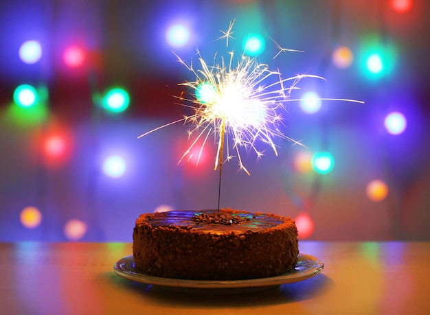 Tasty cake with sparkler on shiny background