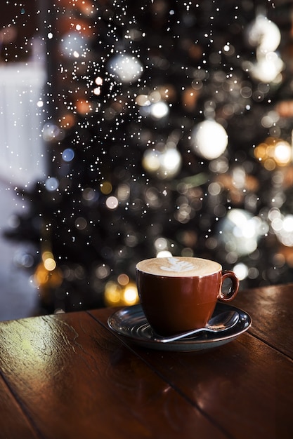 Cappuccino gustoso con alcune luci sfocate sull'albero di natale e sulla neve vacanze concept