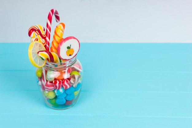 Tasty chewing sweets, bright lollipops with candy cane and jelly candies in the glass can on wooden turquoise board