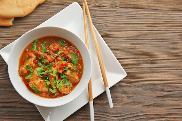 Tasty chicken curry in soup plate and chopsticks on table