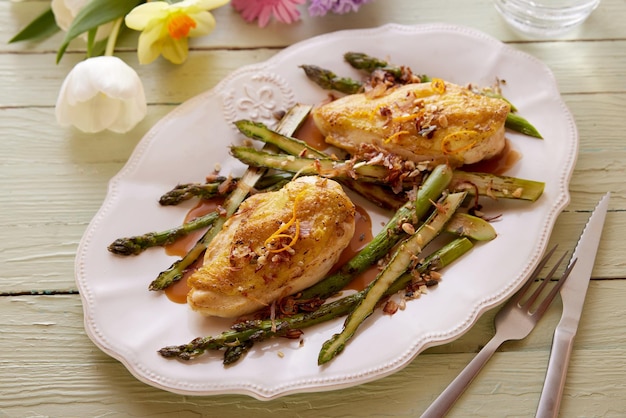 Tasty chicken with asparagus on plate on wooden table