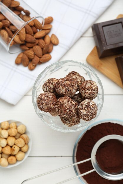 Tasty chocolate balls and ingredients on white wooden table flat lay