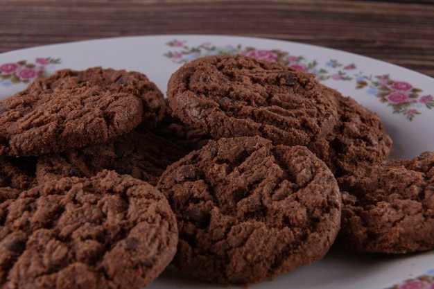 Вкусное печенье с шоколадной крошкой на белой тарелке на деревянном фоне