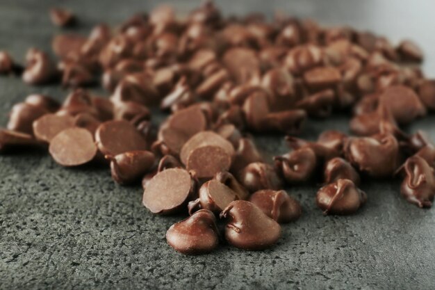 Tasty chocolate chips on dark textured background close up