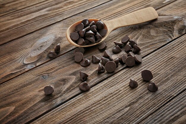 Photo tasty chocolate chips and spoon on wooden background