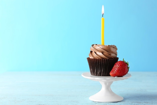 Tasty chocolate cupcake with candle and berry on blue background