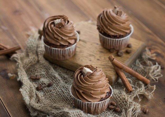 Tasty chocolate cupcakes and sticks of cinnamon on a wooden board Top view