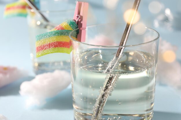 tasty cocktail in glass decorated with gummy candy on light blue background closeup