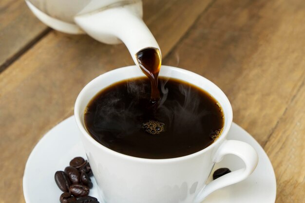 Tasty coffee pouring into white cup on table