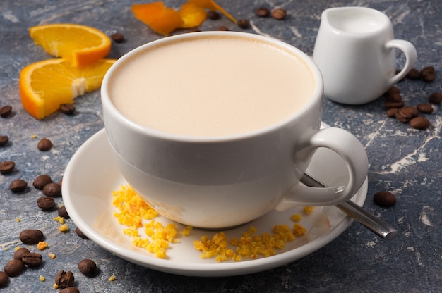 Tasty coffee with milk and oranges on a gray background