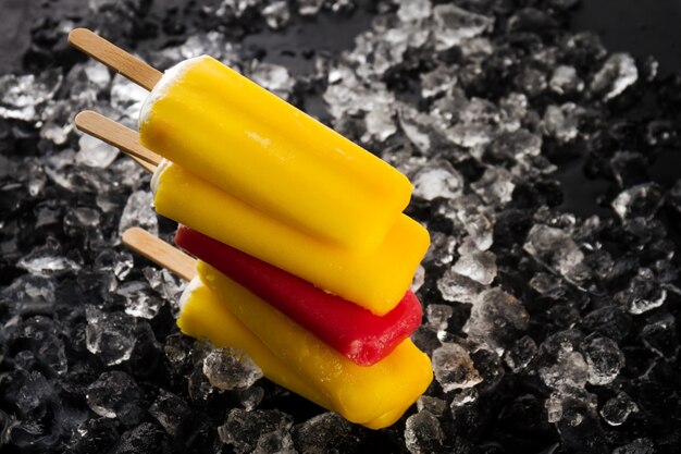 Tasty cold fresh appetizing ice cream on stick on ice cubes on dark background. Closeup.