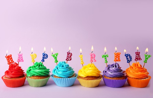 Вкусные красочные кексы со свечами с днем рождения на цветном фоне