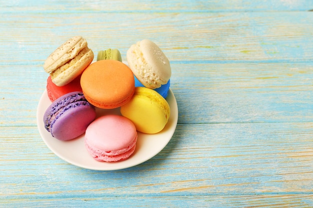 Вкусные красочные миндальное печенье в маленькой тарелке на цветном деревянном фоне