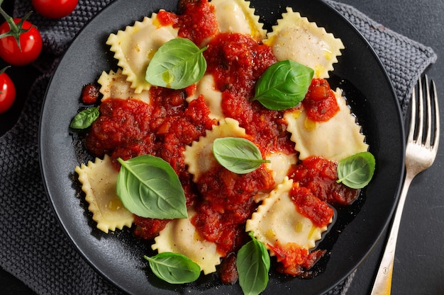 Tasty cooked italian ravioli with tomato sauce and basil served on dark plate.