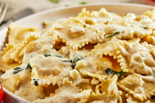 Tasty cooked ravioli with cream sauce, cherry tomatoes, sunflower oil and basil on a light wooden surface