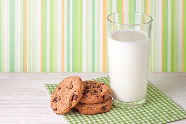 Tasty cookies and glass of milk on white wooden surface and colorful background