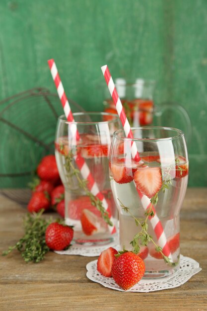 Tasty cool beverage with strawberries and thyme on wooden background