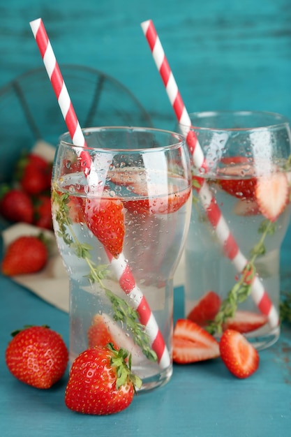 Tasty cool beverage with strawberries and thyme on wooden background