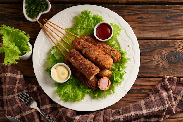 Tasty corn dog with sauce and salad served on white plate on wooden table