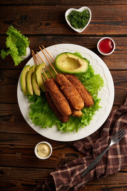 Tasty corn dog with sauce and salad served on white plate on\
wooden table