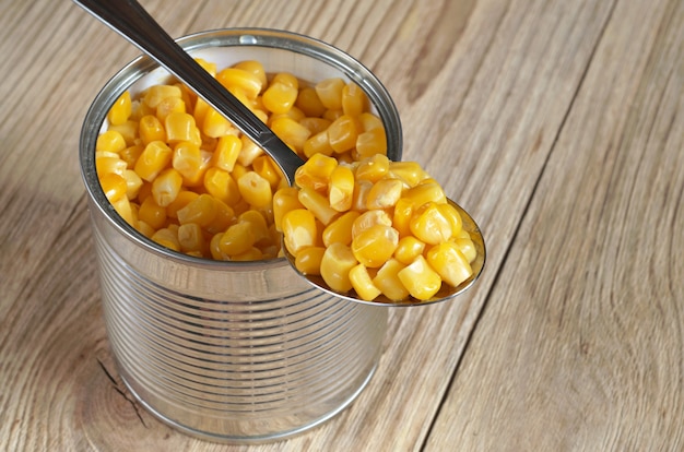 Tasty corn grain in spoon and can on old wooden table