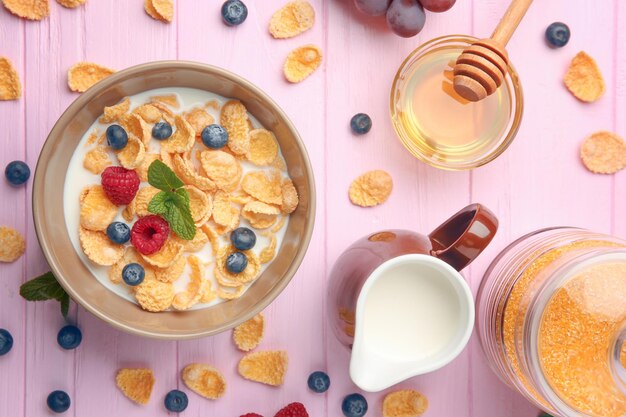 Tasty cornflakes with raspberries and blueberries on pink background