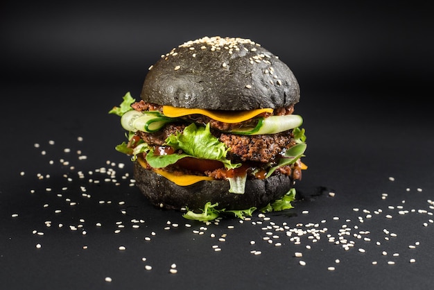 Фото Вкусный бургер с черной булочкой на черном фоне