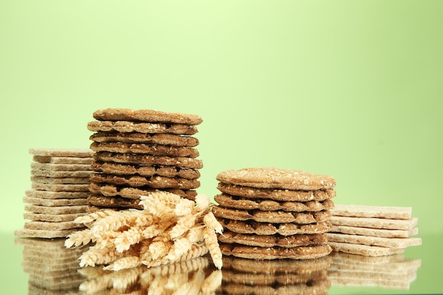 Tasty crispbread and ears on green background