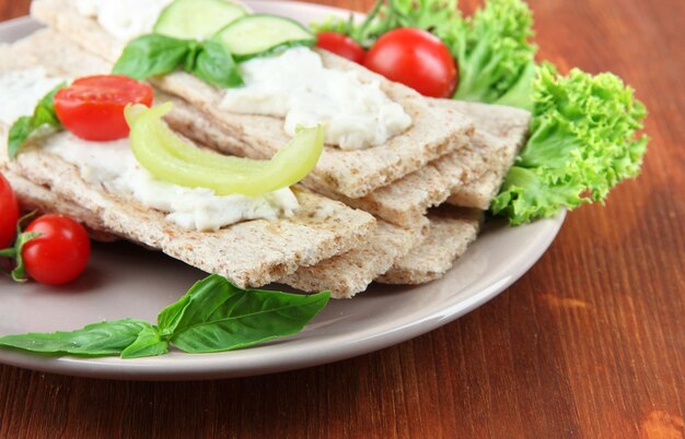 Tasty crispbreads with vegetables on wooden background