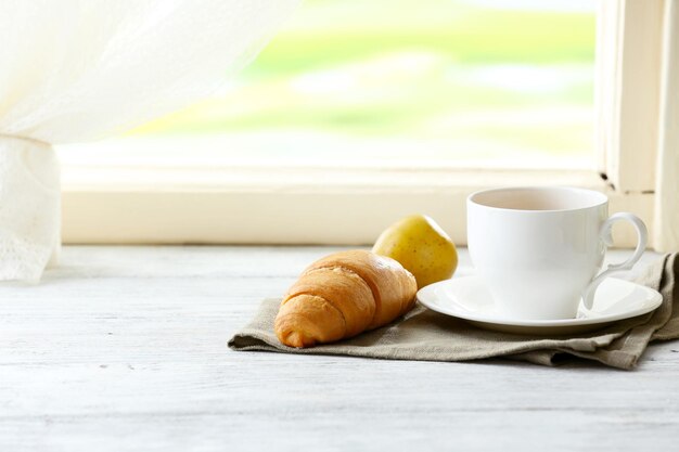 Foto un croissant gustoso e una tazza di tè su un tovagliolo su uno sfondo chiaro